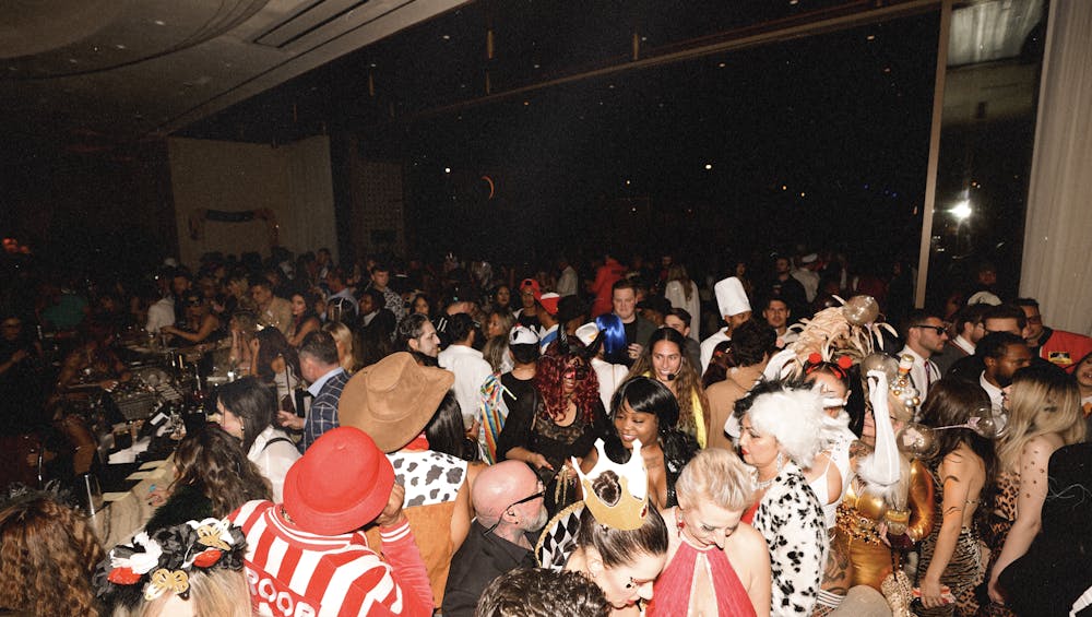 Packed dance floor at Bel-Aire Lounge during a Halloween party. Dozens of guests in costumes including cowboys, Cruella de Vil, and colorful wigs crowd the bar and mingle under dim nightlife lighting.