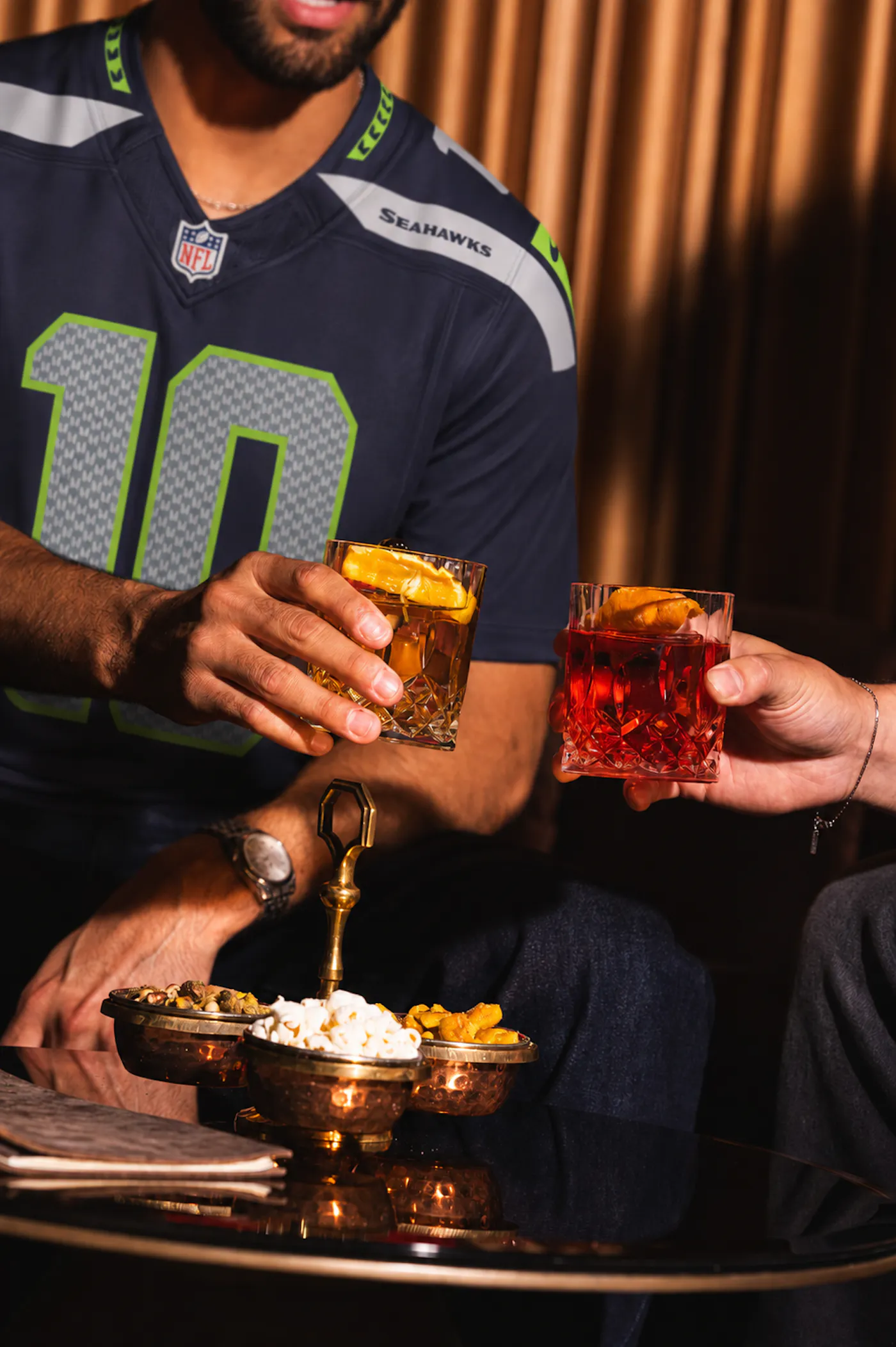Football fans in a Seahawks jersey raising cocktails at Clique Bar & Lounge