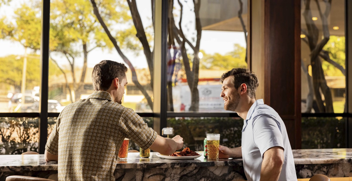 two men sitting at a table with drinks and food