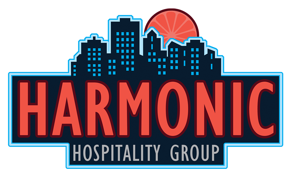 Harmonic Hospitality Group logo in full color featuring a dark blue city skyline silhouette and a pink citrus slice sun.