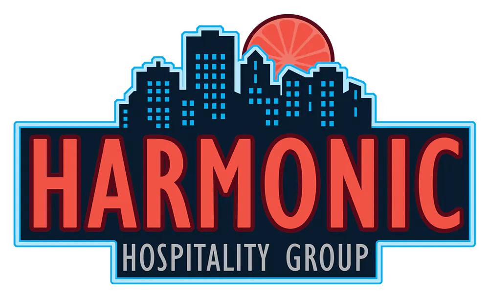 Harmonic Hospitality Group logo in full color featuring a dark blue city skyline silhouette and a pink citrus slice sun.