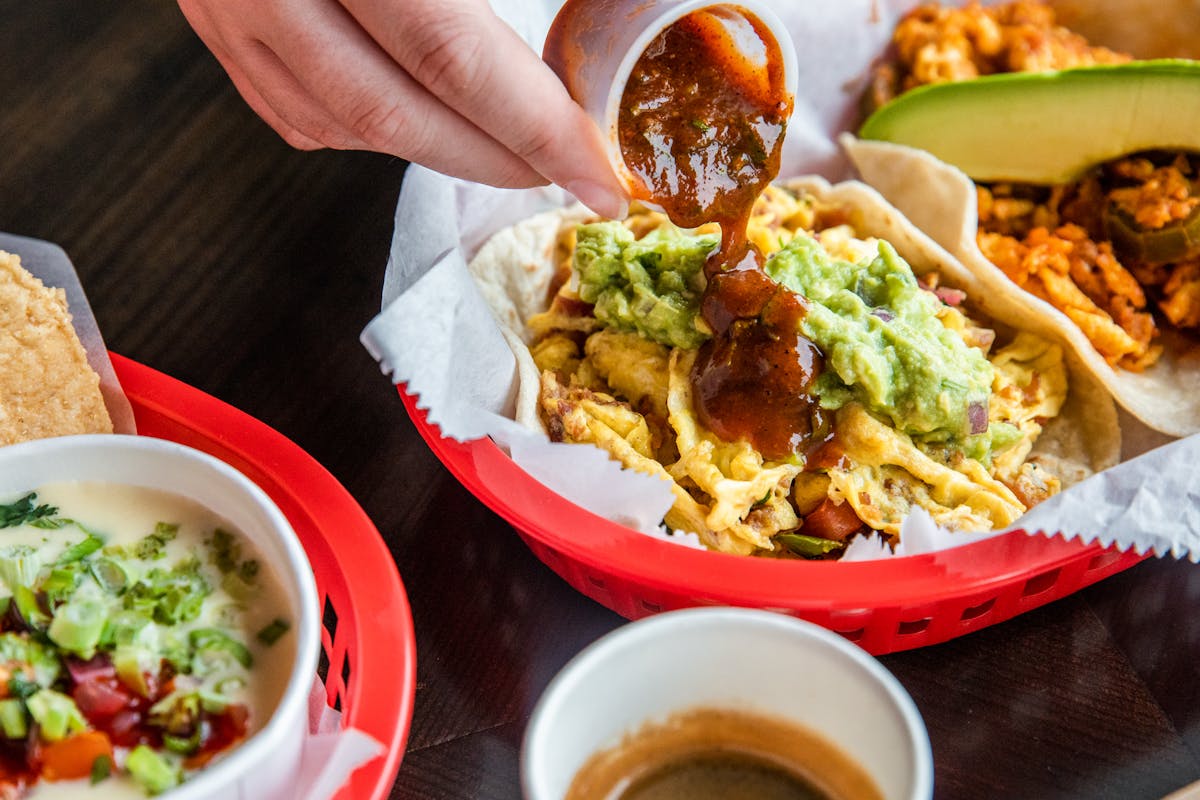 A person pouring salsa over a breakfast taco at Tacos A Go Go
