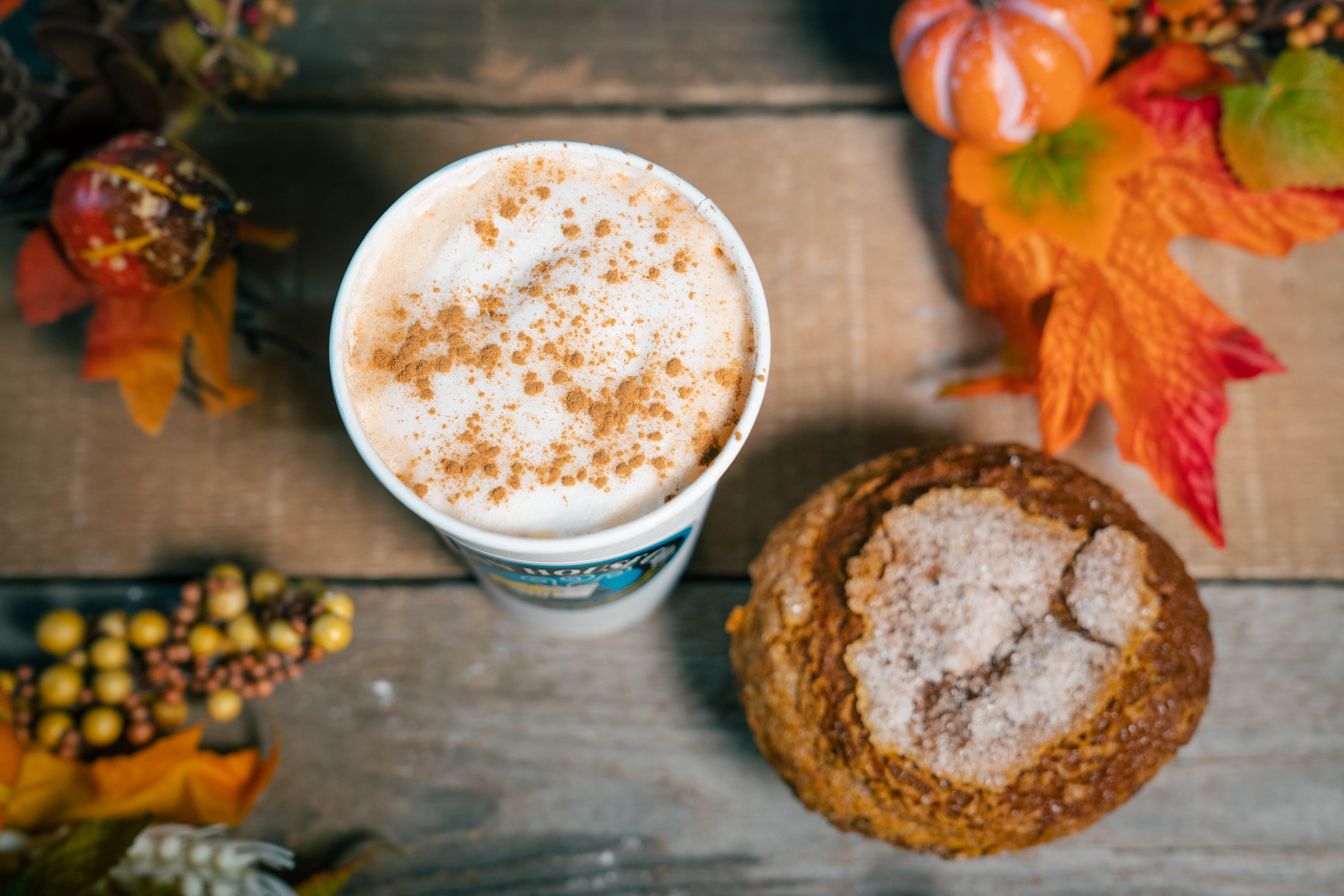 a cup of coffee with a cookie and a pumpkin spiced pastry
