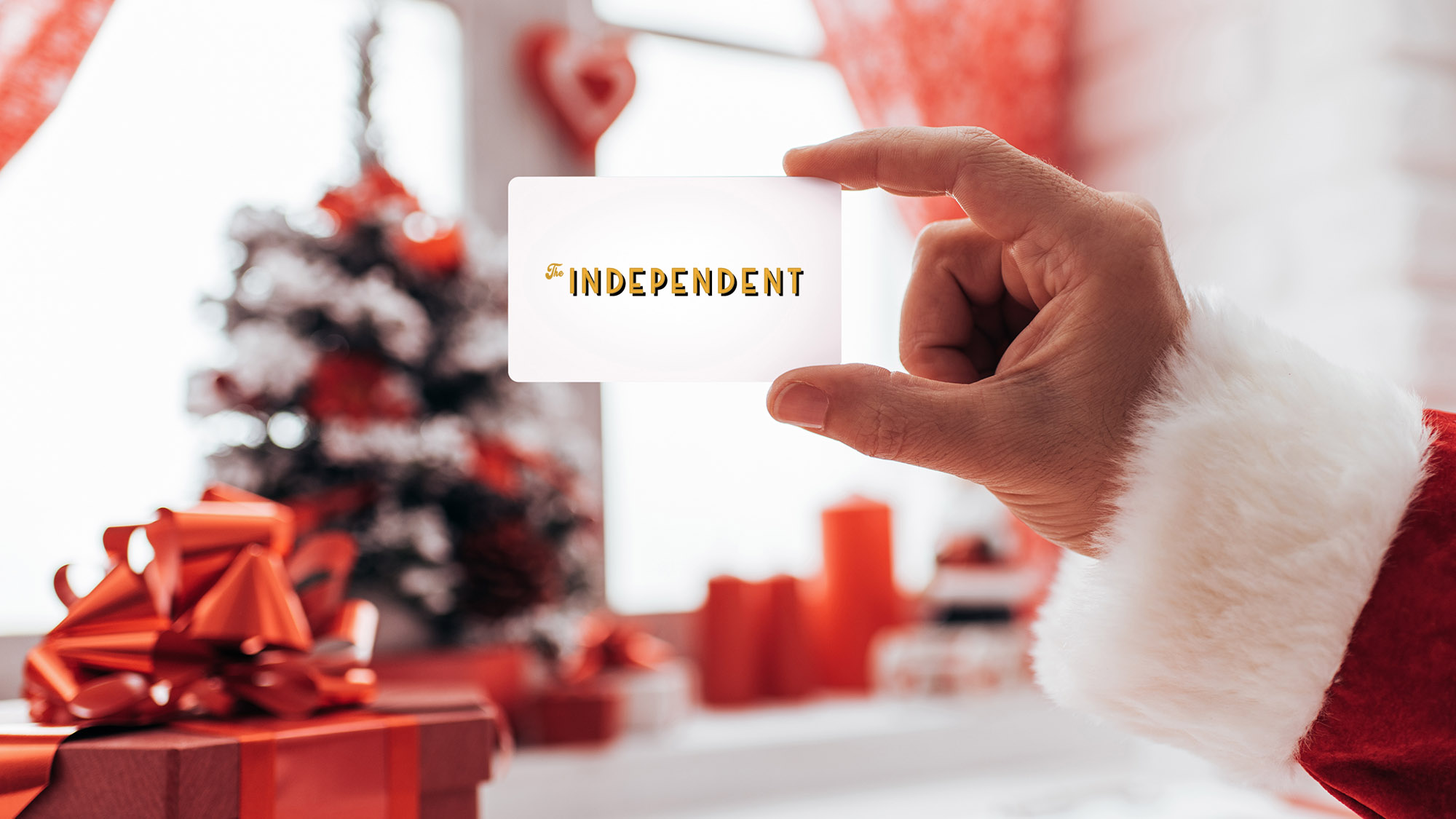 Santa holding The Independent's gift card with a Christmas tree and presents in the background
