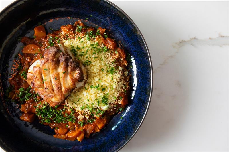 Grilled salmon over green herb couscous in a deep blue bowl with charred citrus garnish.rouper with couscous at Tzeva in Sarasota