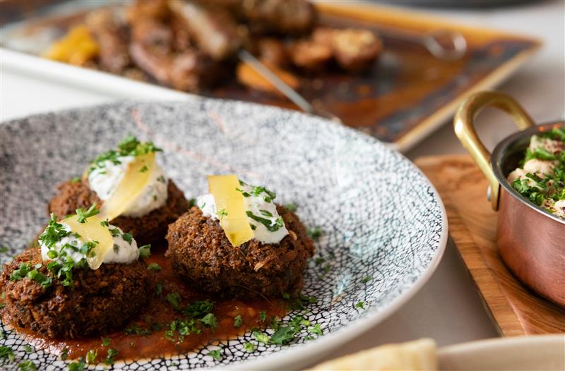 Crispy falafel balls topped with herb garnish, served over creamy sauce with crispy onions.
