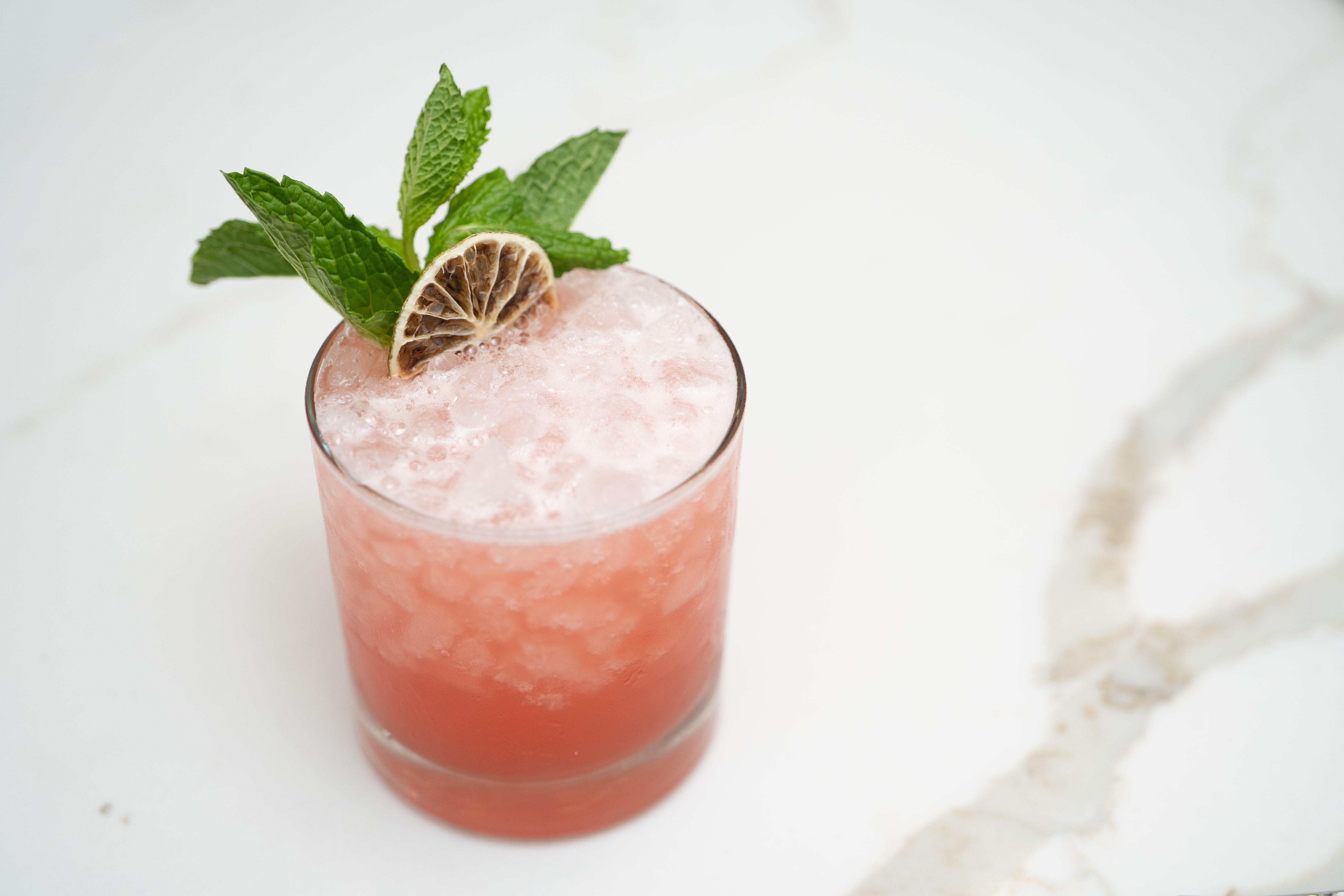 Pink citrus cocktail in a rocks glass with a dehydrated lime garnish on a light marble surface.