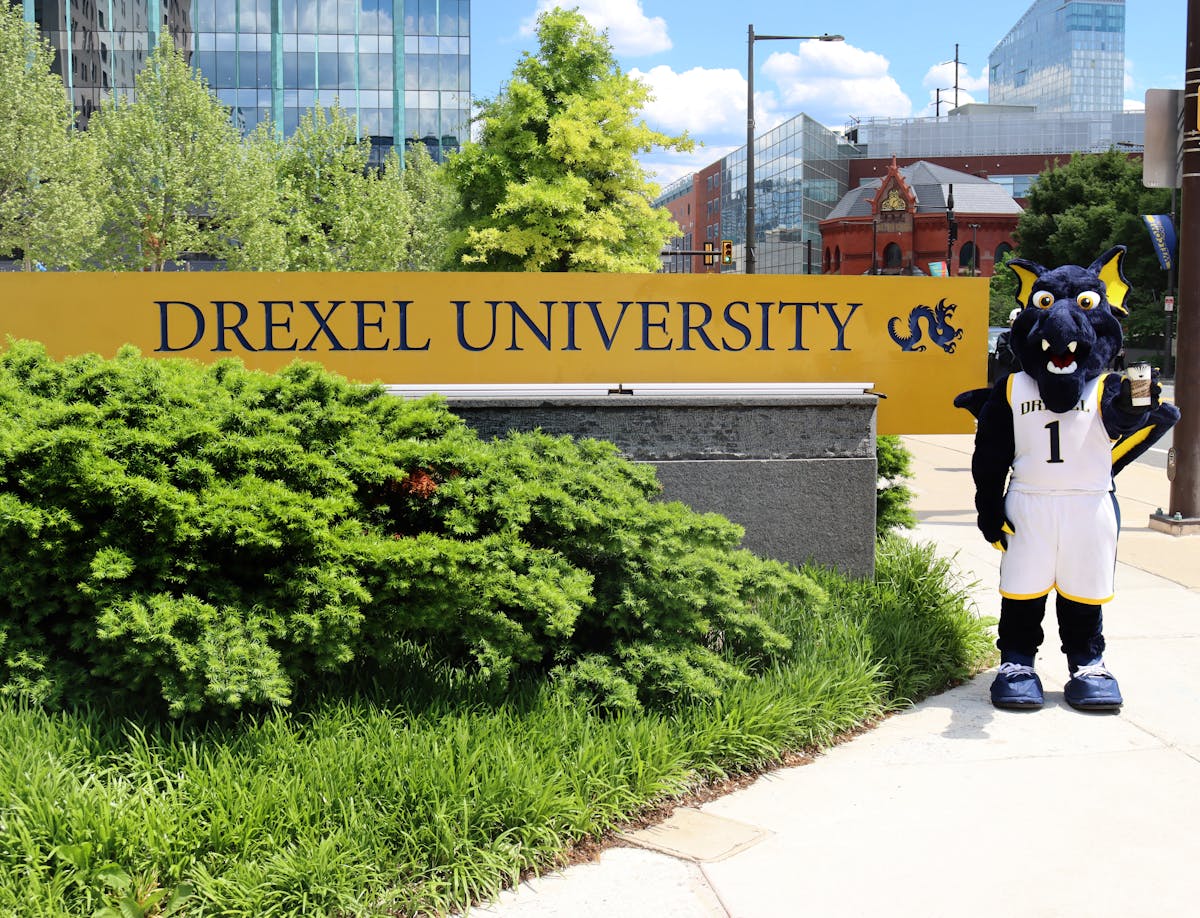 the drexel university mascot holding a Saxbys cup in front of a sign