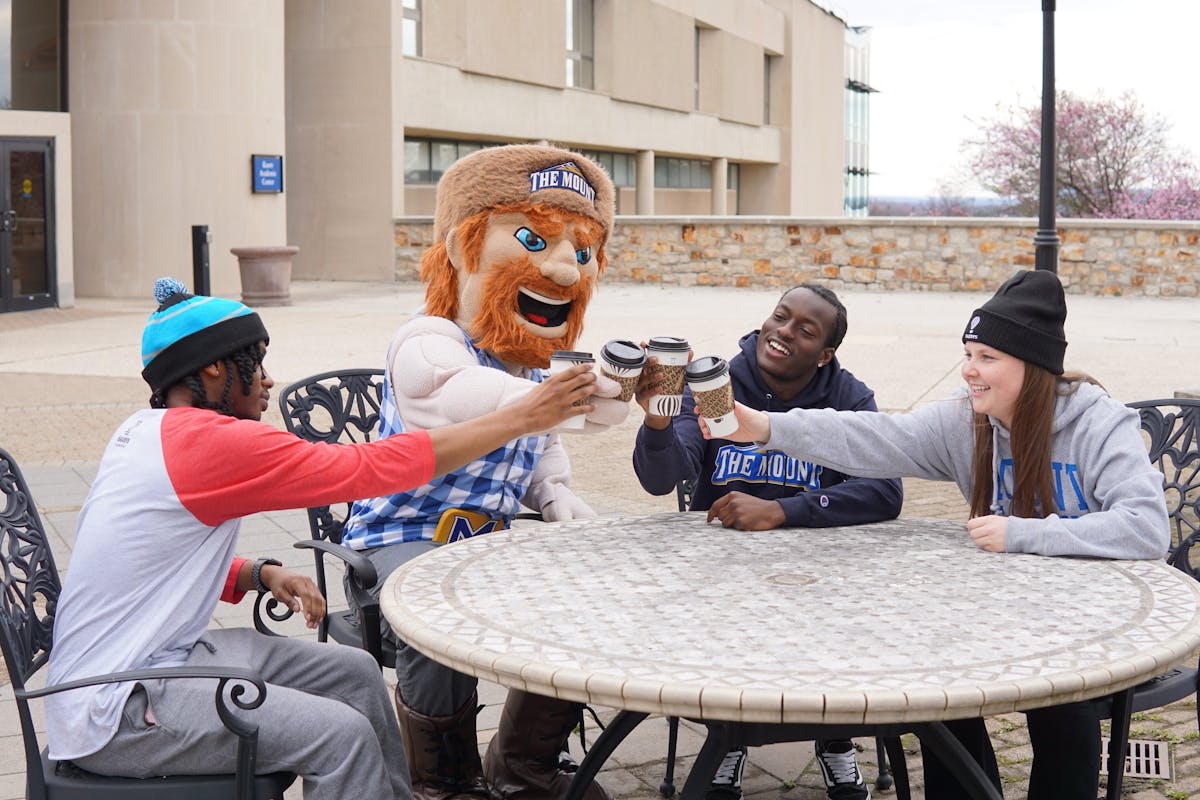 a group of people and a mascot cheersing a cup of Saxbys coffee around a table