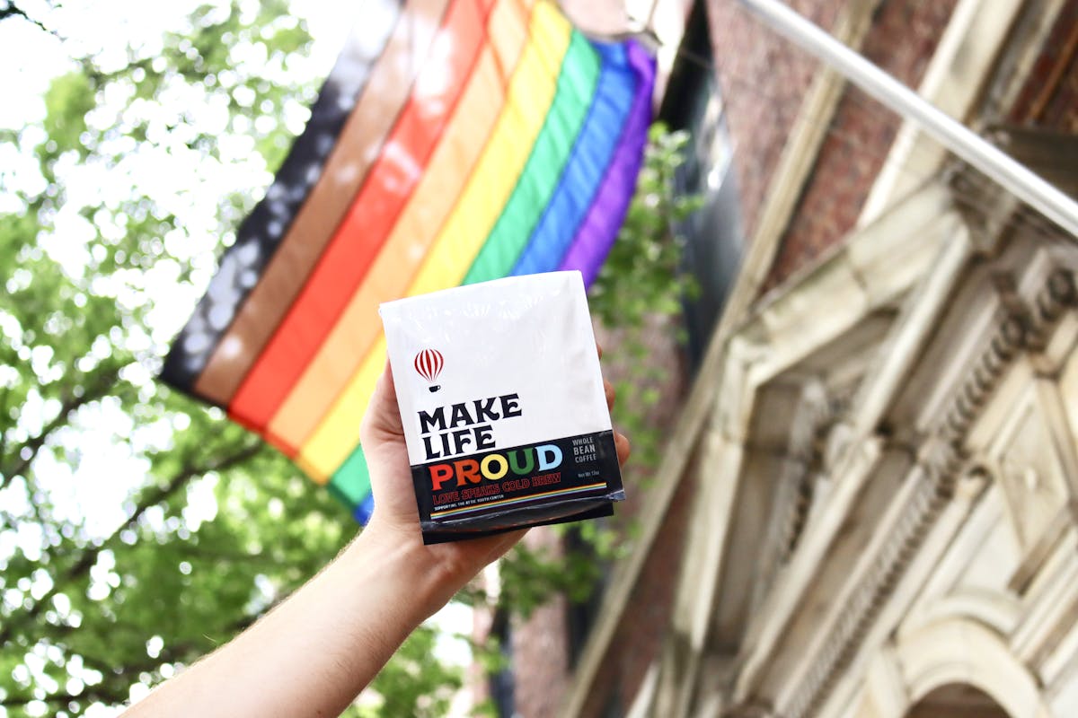 a close up of a person holding a bag of love speaks cold brew in front of a Pride Flag