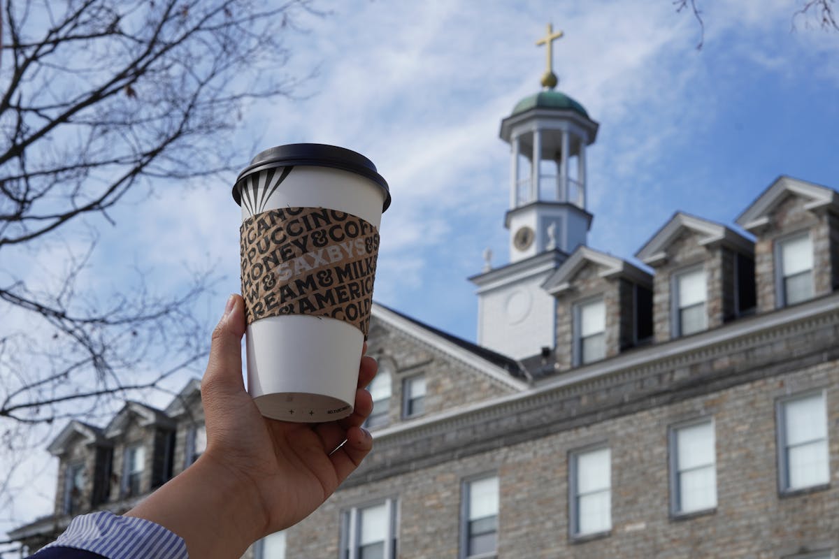 a hand holding a saxbys cup in front of a building
