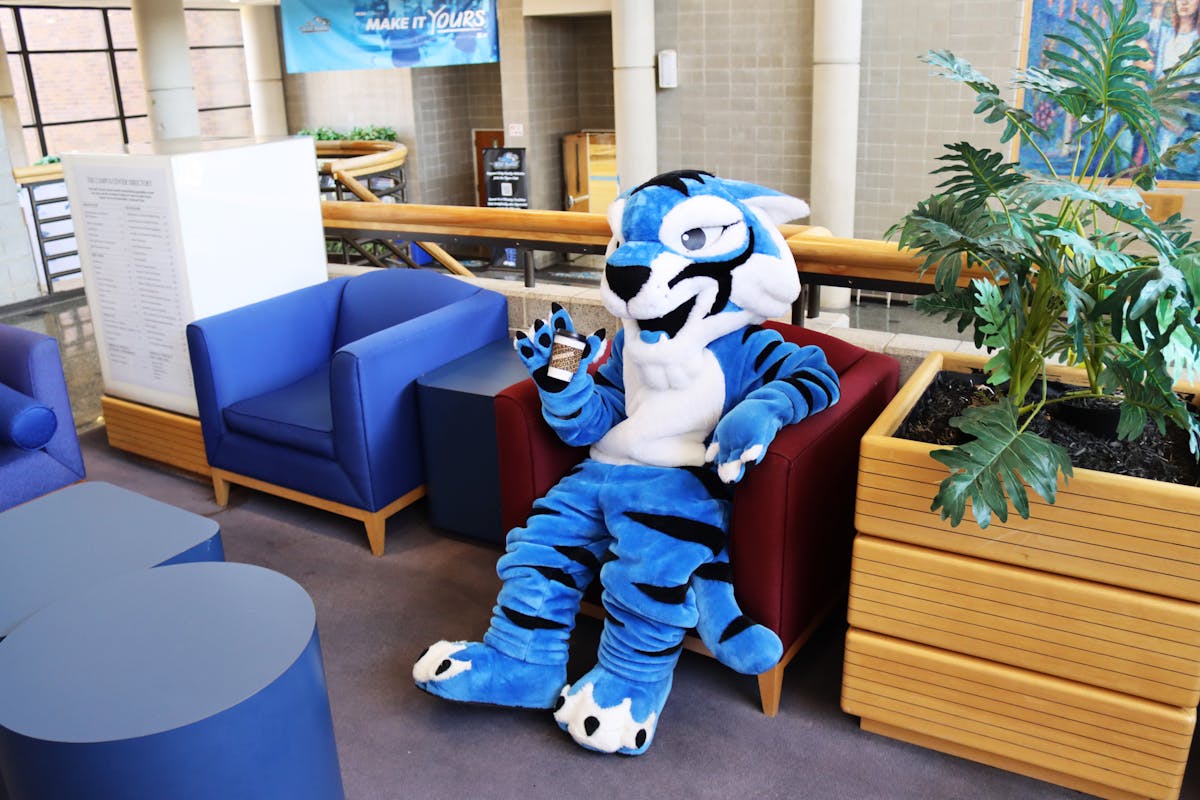 a mascot holding a saxbys cup sitting in a chair