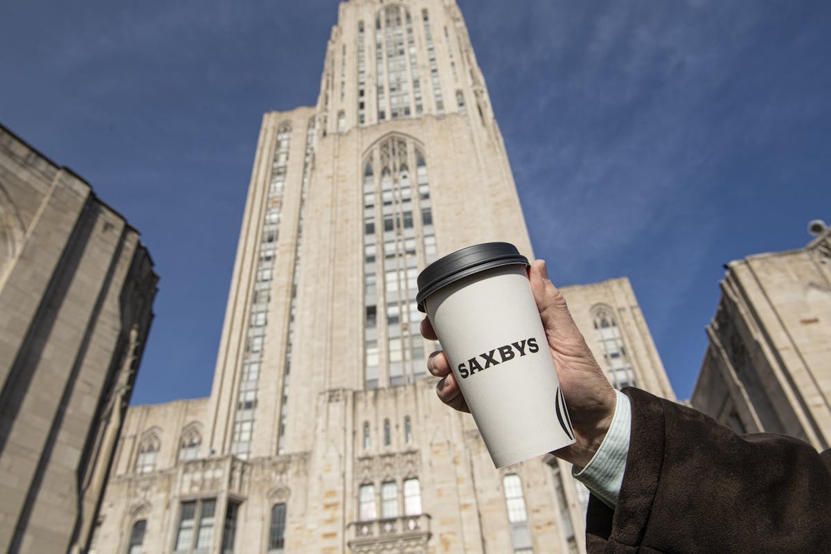 a hand holding a cup of coffee in the air in front of a tall building