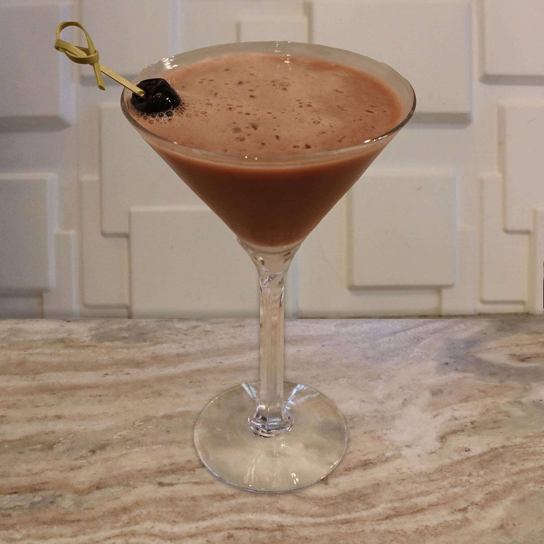A deep, dark reddish-brown chocolate cherry cocktail garnished with a dark cherry.