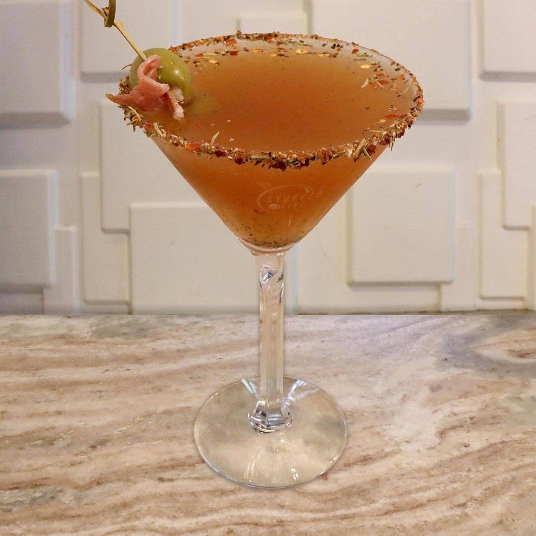 A rich, opaque red tomato-based cocktail featuring a heavily seasoned spice rim, garnished with a green olive.