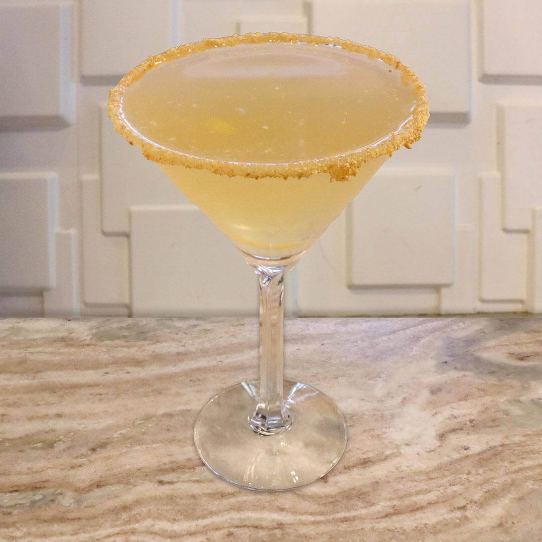 A bright yellow honey-colored cocktail featuring a crumbly graham cracker rim.