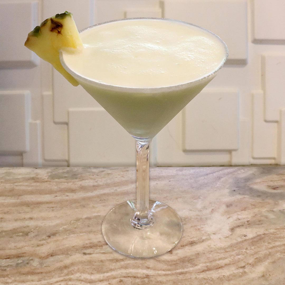 A creamy, pale green tropical cocktail served in a chilled glass, garnished with a pineapple wedge.