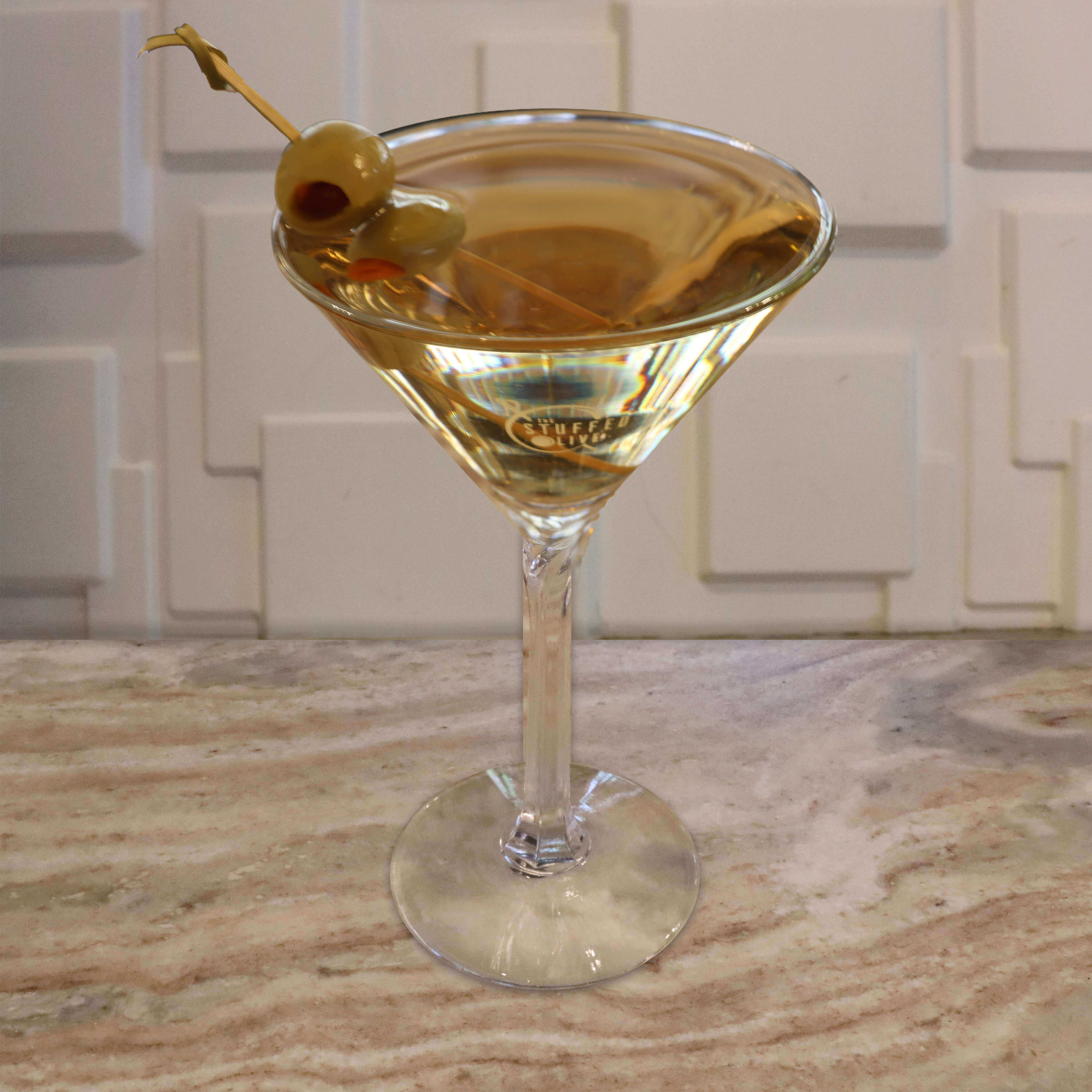 A clear, spirit-forward cocktail garnished with a green pimento-stuffed olive.