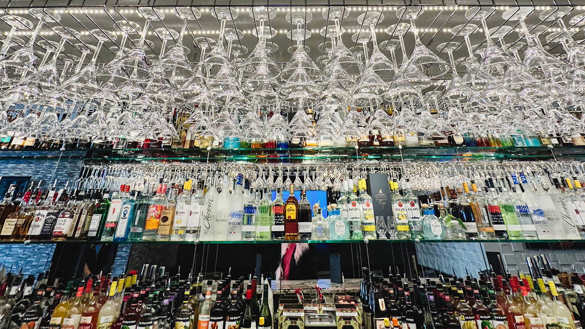 Close-up shot of hundreds of martini glasses hanging above the back bar at The Stuffed Olive in Iowa City, with a varied liquor selection visible on shelves below.
