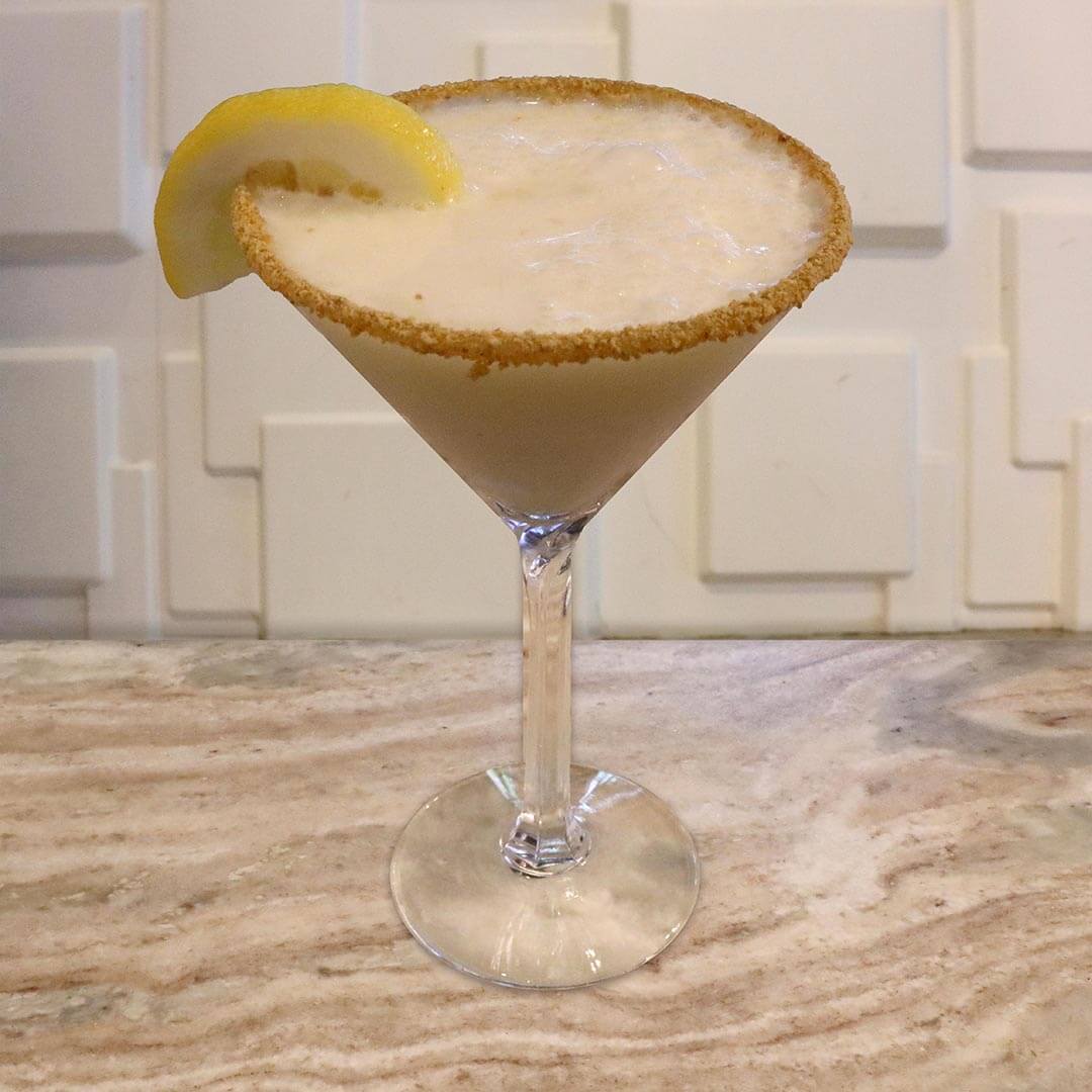 A creamy yellow cocktail featuring a toasted graham cracker rim, topped with a lemon garnish.
