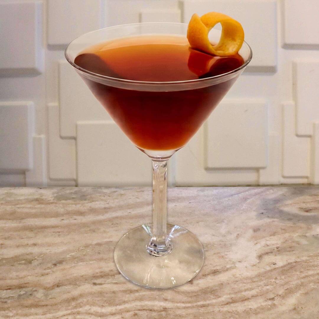 A rich, dark amber cocktail served in a classic glass, elegantly garnished with a thick, curled orange peel.
