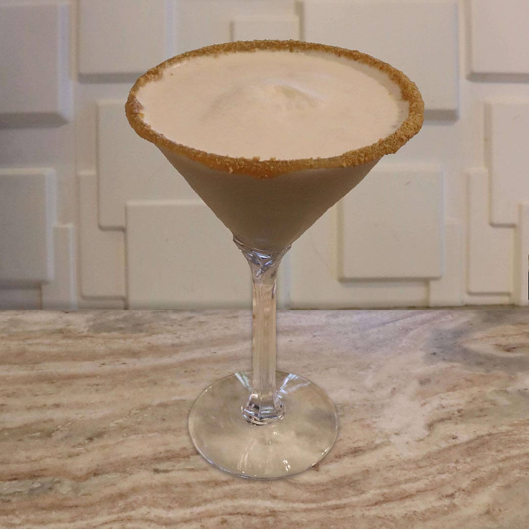 A creamy, golden-tan cocktail served in a glass featuring a thick caramel and crushed graham cracker rim.