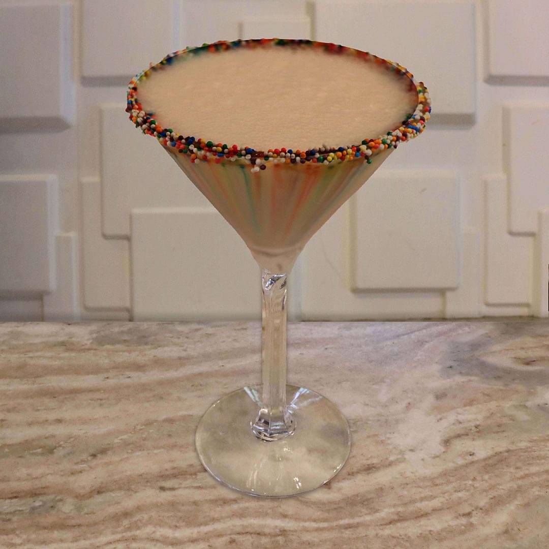 A creamy, light brown chocolate cocktail featuring a brightly colored rainbow sprinkle rim.