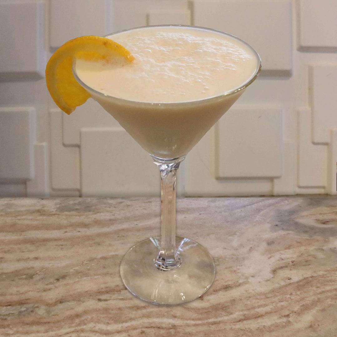 A creamy, pale orange-yellow cocktail served in a glass, garnished with an orange slice.
