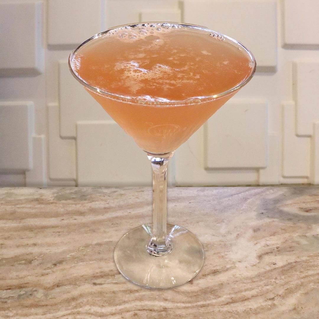 A cloudy pink pomegranate cocktail served in a chilled glass.