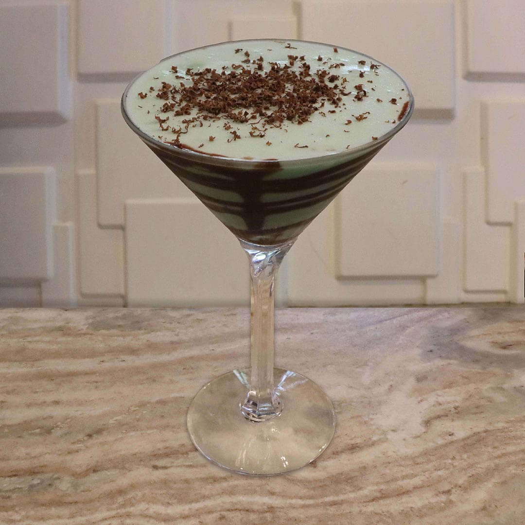 A creamy, pale mint-green cocktail with chocolate swirls in the glass, topped with freshly shaved chocolate.