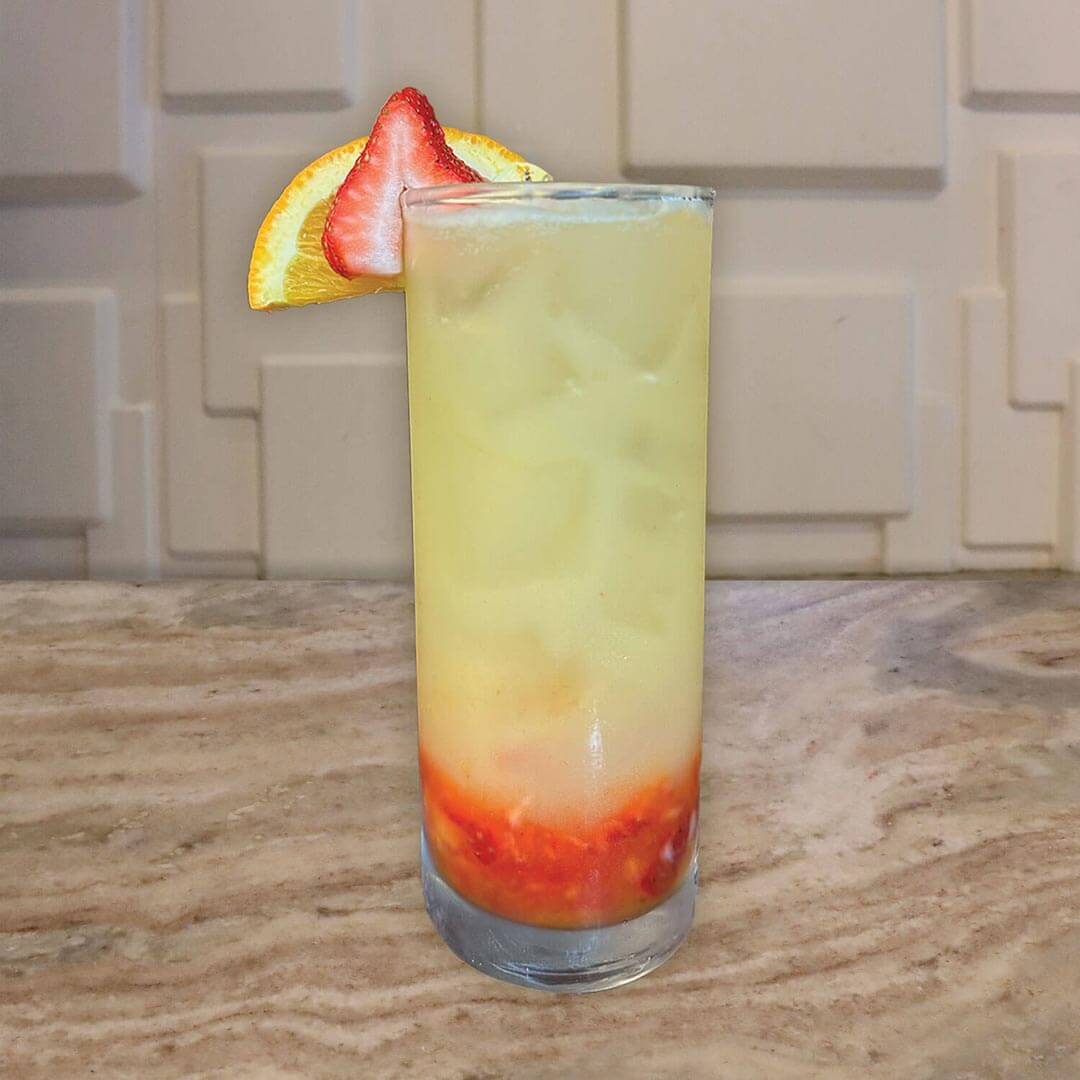A tall layered beverage with a yellow-to-red gradient and a lime garnish.
