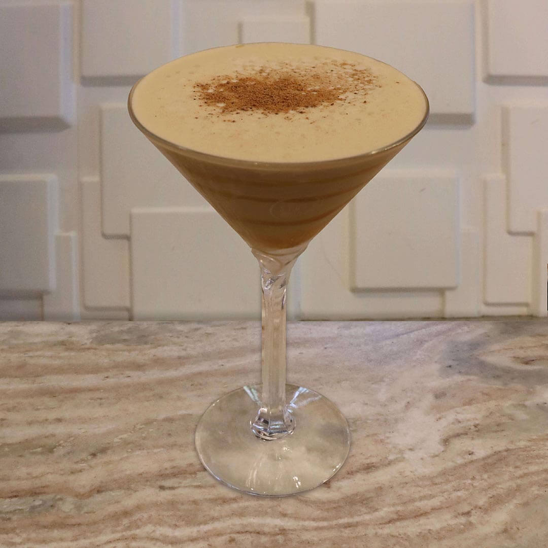 A creamy, light tan chai cocktail featuring caramel swirls inside the glass and a dusting of nutmeg on top.