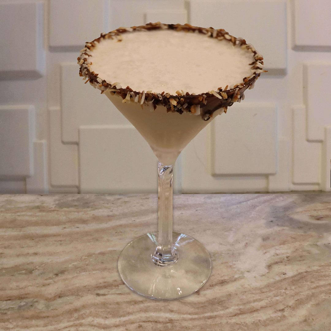 A creamy, light brown chocolate cocktail served in a glass with a thick, toasted coconut rim.