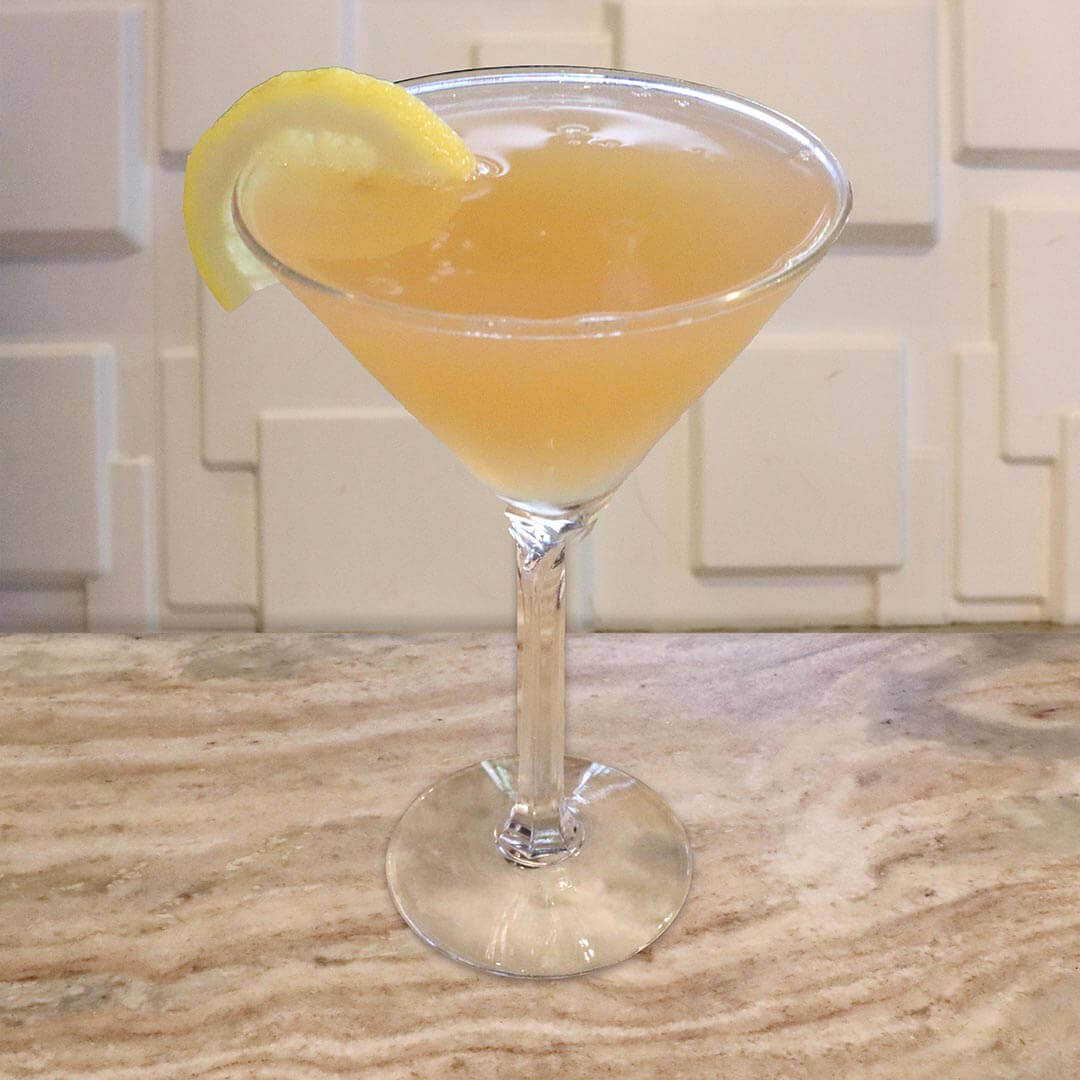 A pale, cloudy yellow citrus cocktail served in a chilled glass, garnished with a lemon wedge.