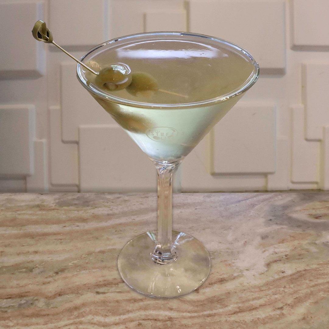 A clear cocktail in a chilled glass, prominently garnished with green olives on a pick.