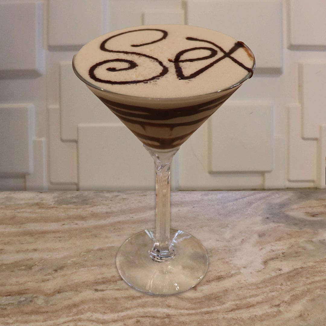 A creamy, light tan cocktail featuring rich chocolate swirls coating the inside of the glass.