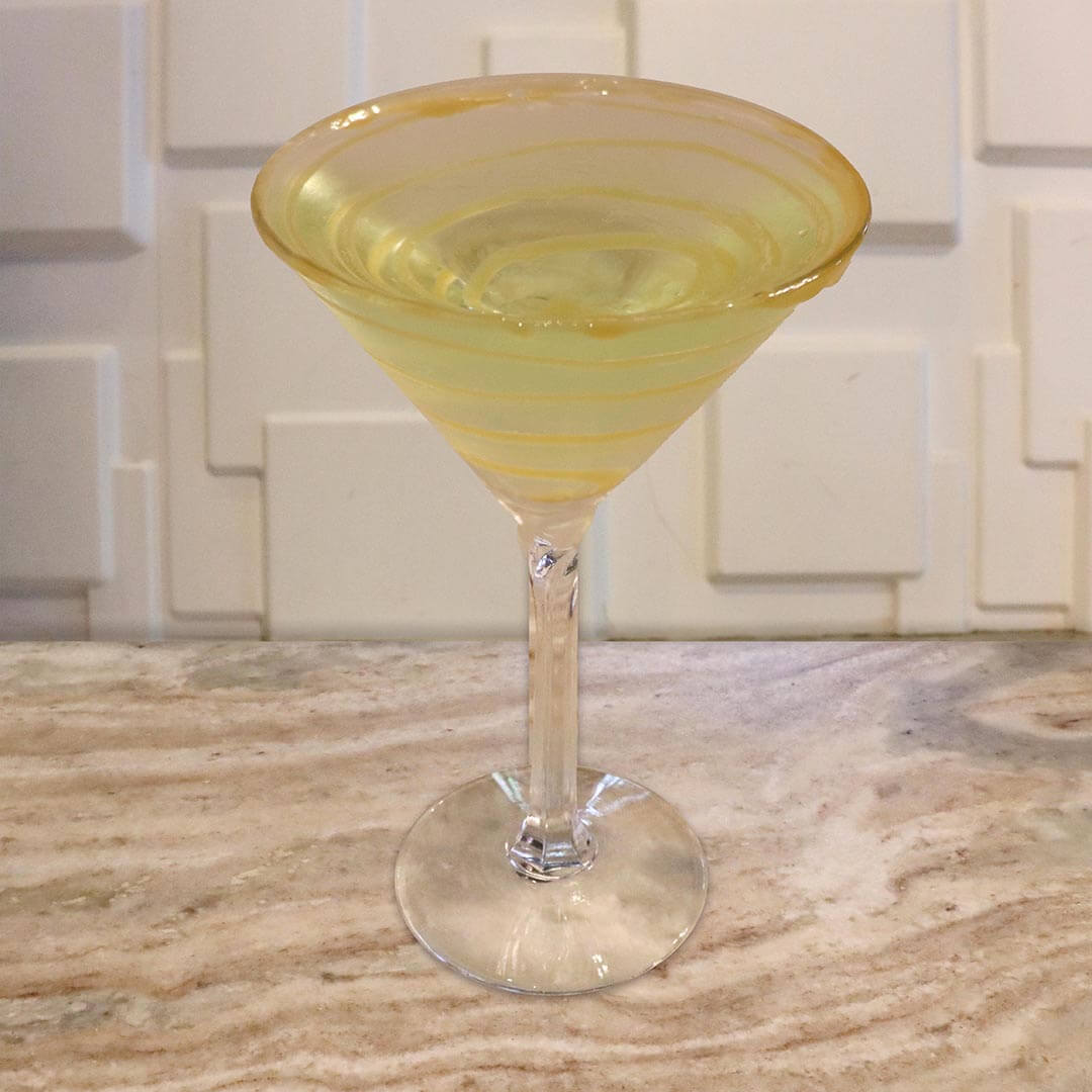A pale yellow-green cocktail featuring a thick caramel-coated rim and caramel swirls inside the glass.