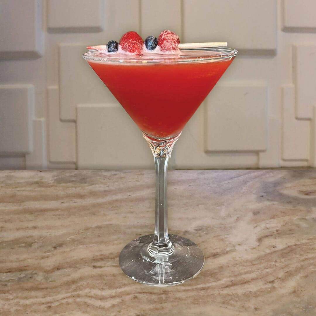 A bright red beverage garnished with fresh blueberries and raspberries.