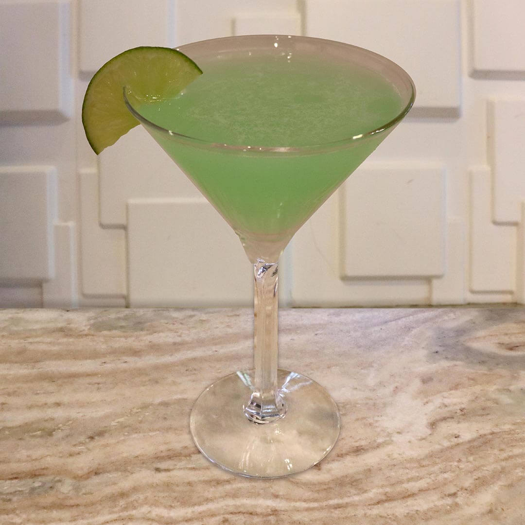 A bright, neon green tropical cocktail served in a chilled glass, garnished with a lime wheel.