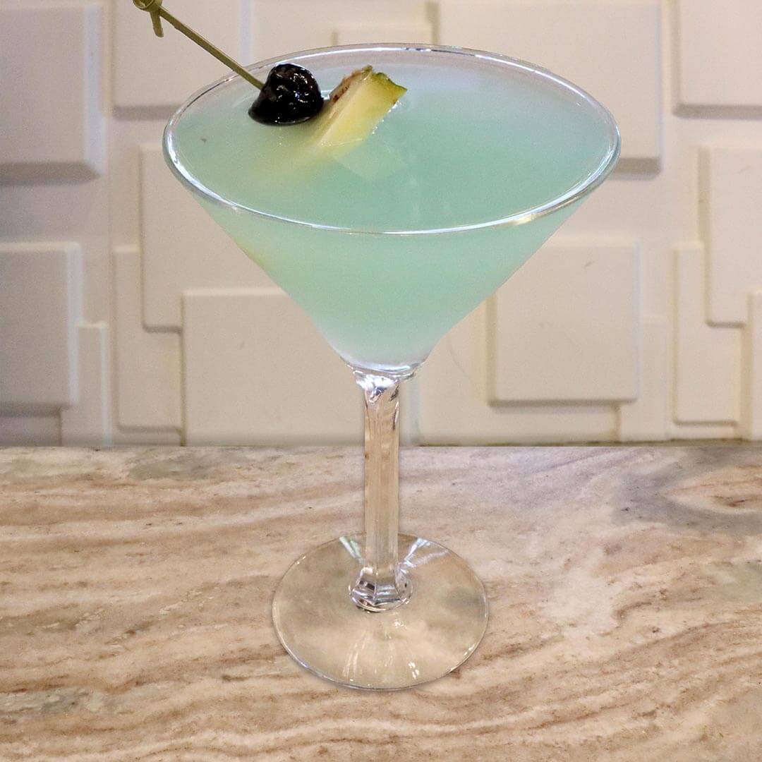 A bright tropical teal cocktail garnished with a dark cherry.