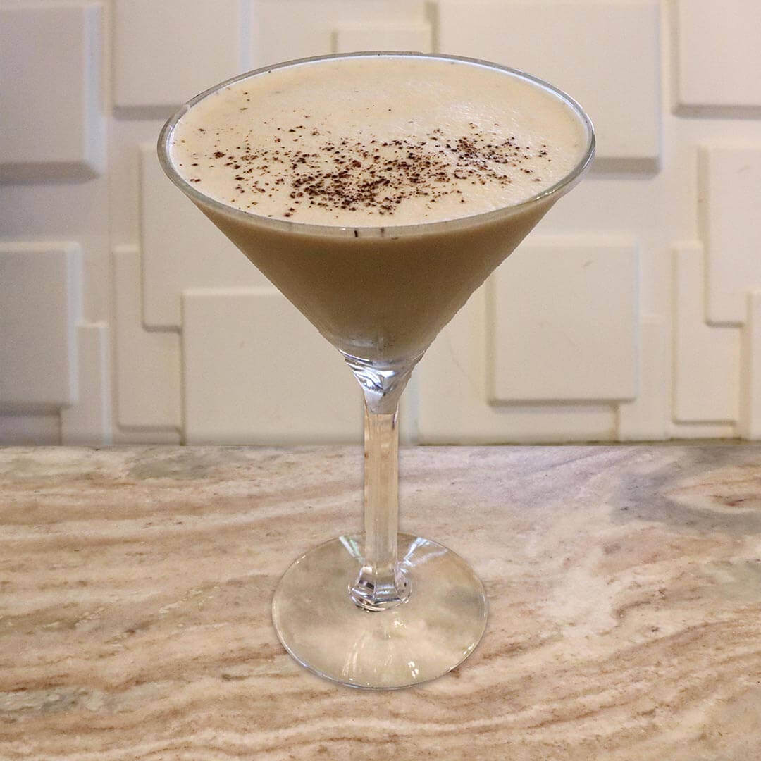 A creamy, coffee-colored cocktail featuring a sprinkle of dark chocolate shavings on top.