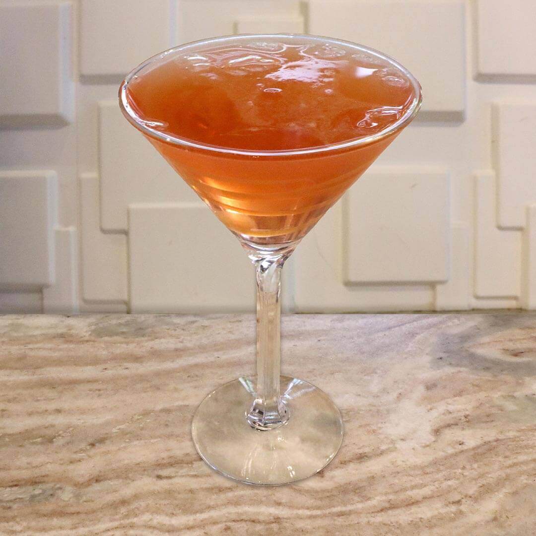 A bright orange-red apple cocktail featuring thick caramel swirls.