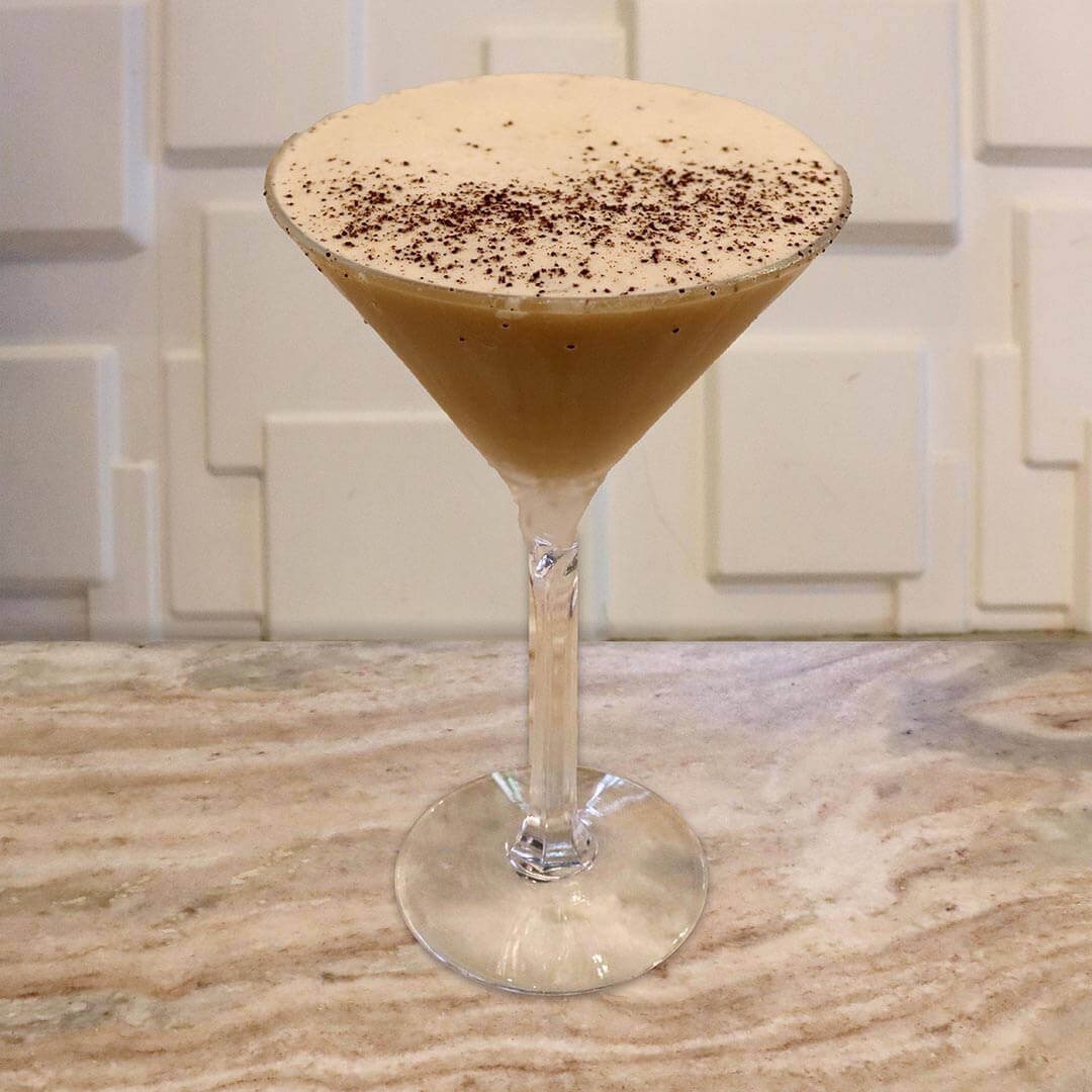 A creamy, light brown espresso-style cocktail topped with light foam and a dusting of nutmeg.