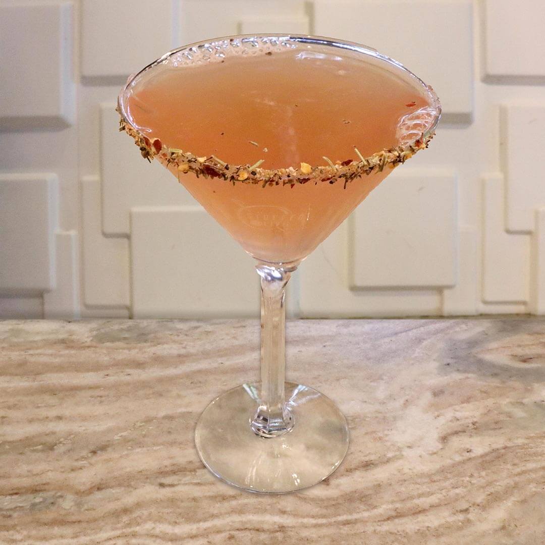 A soft pink-red tropical cocktail served in a glass featuring a garnished rim.