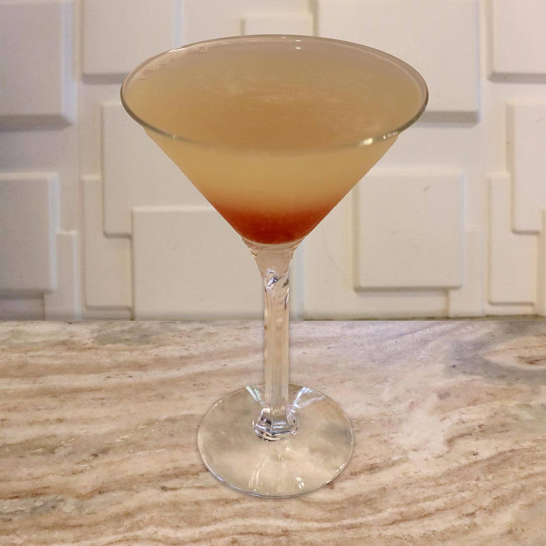 A pale yellow cocktail with a bright red splash at the bottom of the glass.