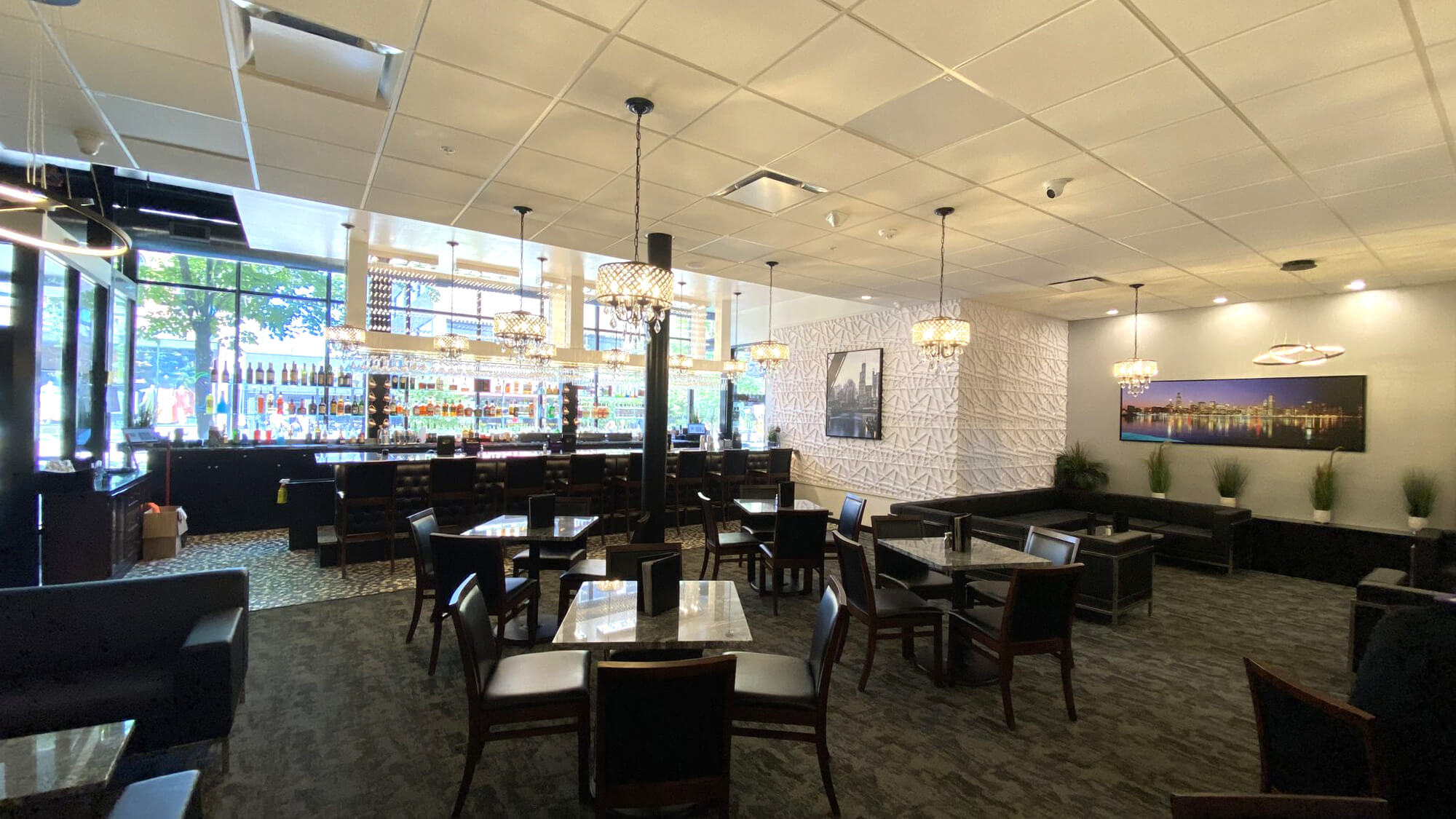 Wide interior view of The Stuffed Olive in Iowa City, showcasing the elegant dining area with marble tables, a fully stocked bar, crystal chandeliers, and a skyline mural.