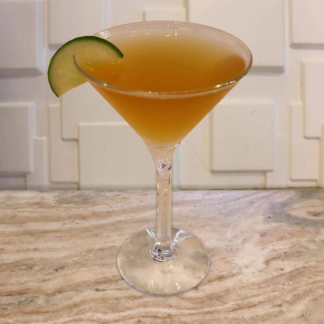 A pale, hazy yellowish-green cocktail in a chilled glass, garnished with a lime slice.