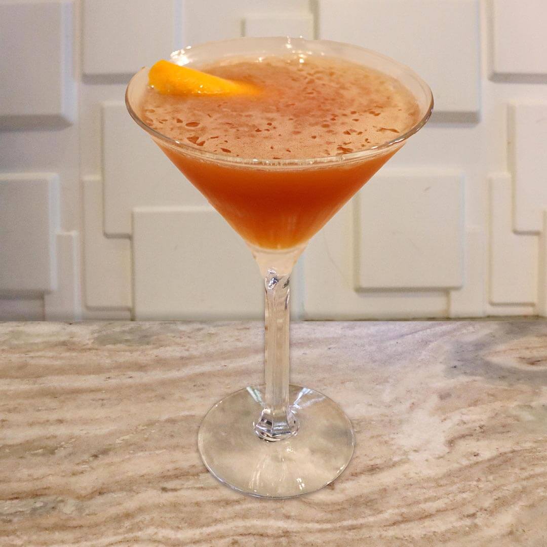 A deep crimson-orange cocktail in a chilled glass, elegantly garnished with an orange twist.