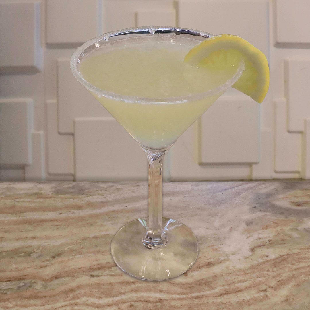 A bright yellow citrus cocktail served in a glass featuring a sugared rim and a fresh lemon wedge.