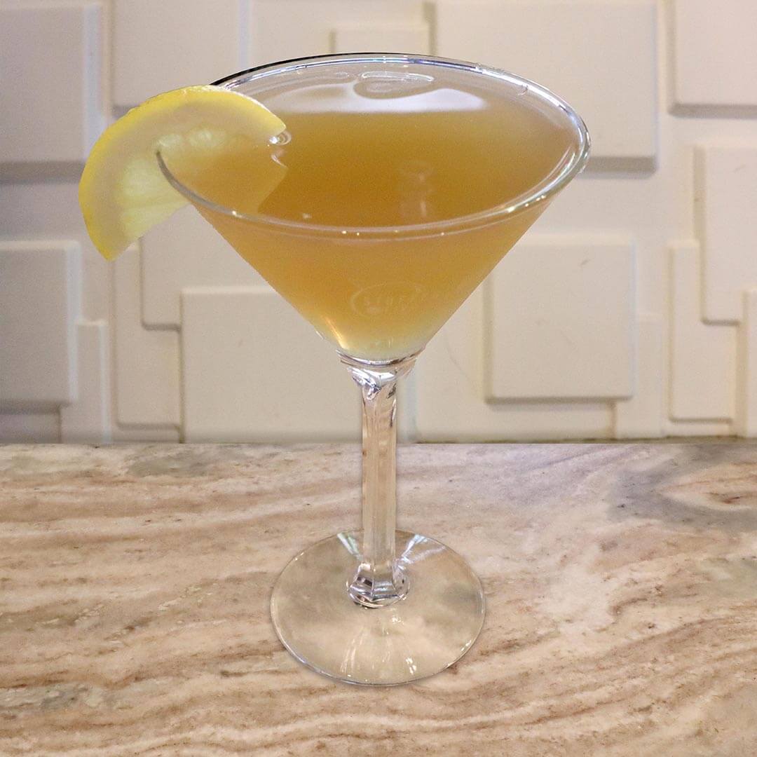A pale gold, tea-colored cocktail served in a chilled glass, garnished with a lemon wedge.